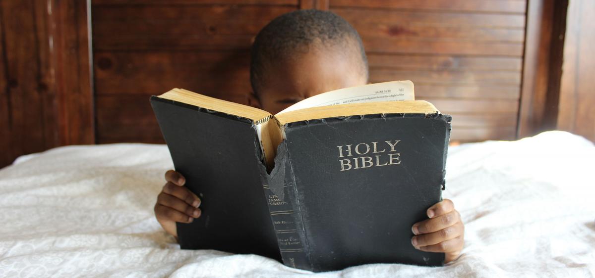 Small child reading a worn Bible