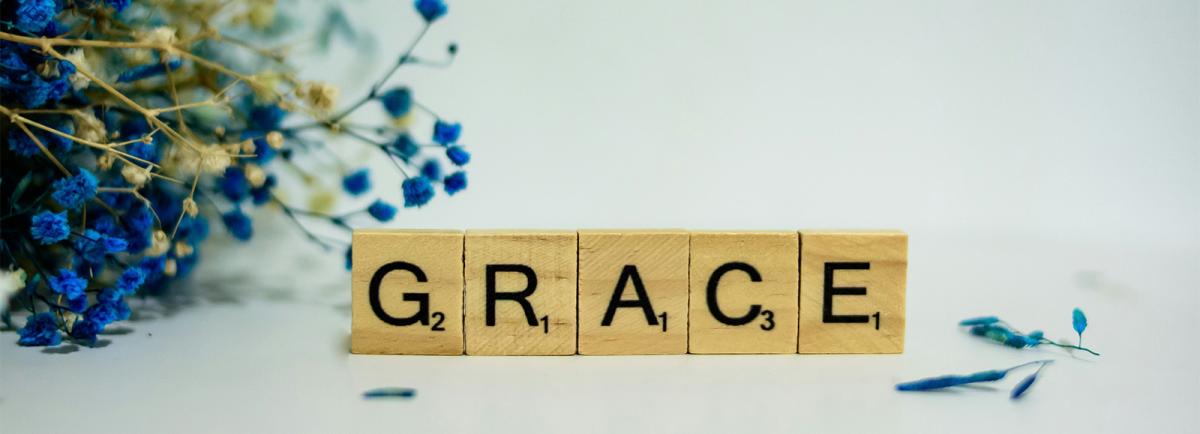 The word Grace spelled in wooden Scrabble times surrounded by small blue flowers