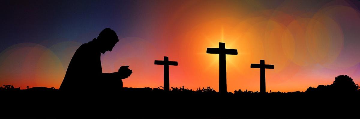 Beautiful sunset and silhouette of man kneeling in prayer in front of three crosses