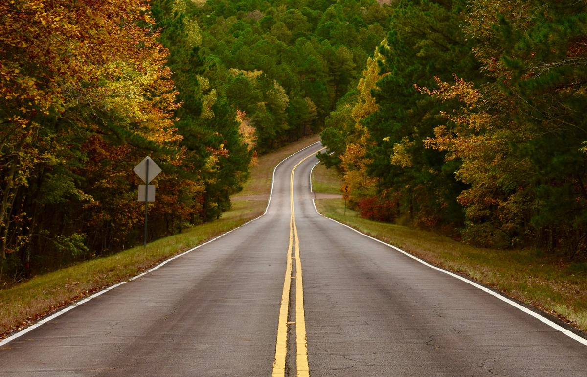 an empty two lane road surrounded by trees filled with fall leaves