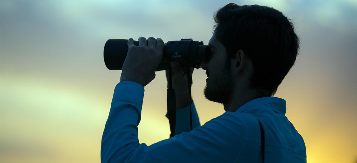 A dark haired man looking through binoculars