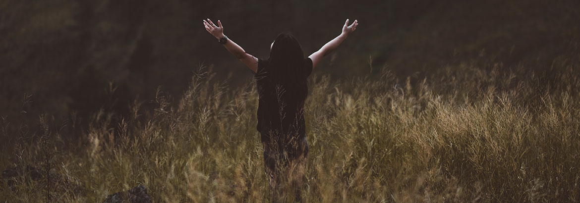 Man in field with arms raised in worship.